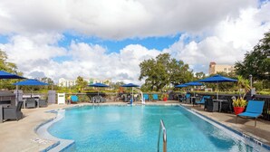 A swimming pool with lounge chairs and umbrellas, surrounded by trees and buildings. - Hampton Inn Orlando-International Airport (Orlando)