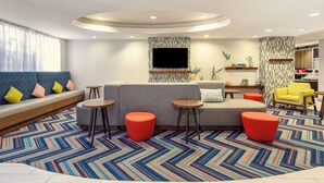 A modern living room with a sofa, ottomans, a flat-screen TV, and a patterned rug. - Hampton Inn Orlando-International Airport (Orlando)