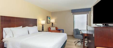 A hotel room with a large bed, a desk with a chair, a television, and a window with a view.