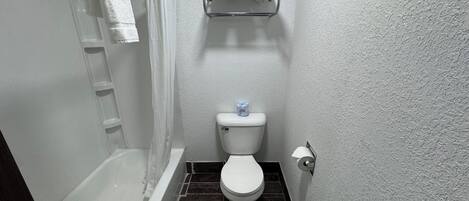 A bathroom with a bathtub, toilet, and a shelf above the toilet.