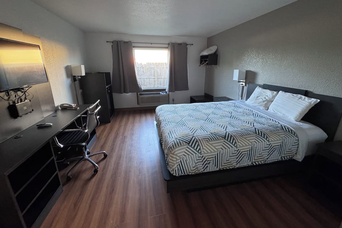 A hotel room with a bed, desk, chair, and a window with curtains.