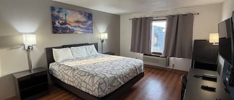 A hotel room with a bed, bedside lamps, a painting, a window with curtains, a desk with a TV, and a radiator.