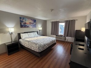 A hotel room with a bed, bedside lamps, a painting, a window with curtains, a desk with a TV, and a radiator. - Best Nights Hotel (Fond du Lac)