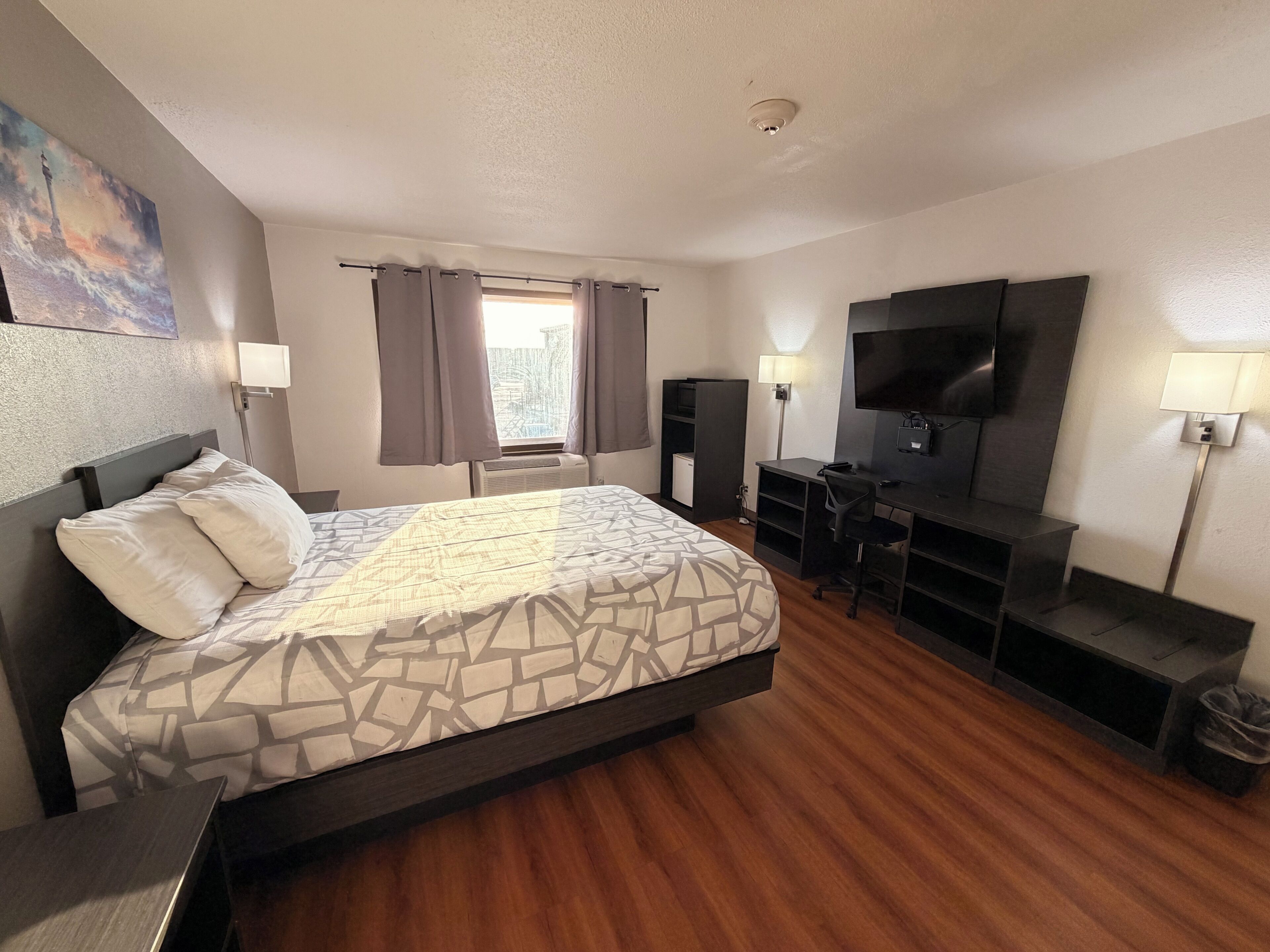 Una habitación de hotel con una cama, un escritorio, un televisor y una ventana con cortinas.