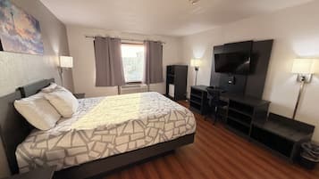 Una habitación de hotel con una cama, un escritorio, un televisor y una ventana con cortinas.