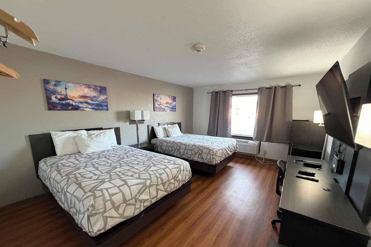 A hotel room with two beds, a TV, a desk, and a window with curtains.