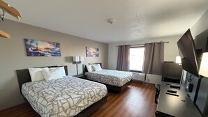 A hotel room with two beds, a TV, a desk, and a window with curtains.
