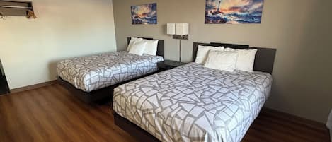 Una habitación de hotel con dos camas, suelo de madera, una mesita de noche, una lámpara y dos cuadros en la pared.
