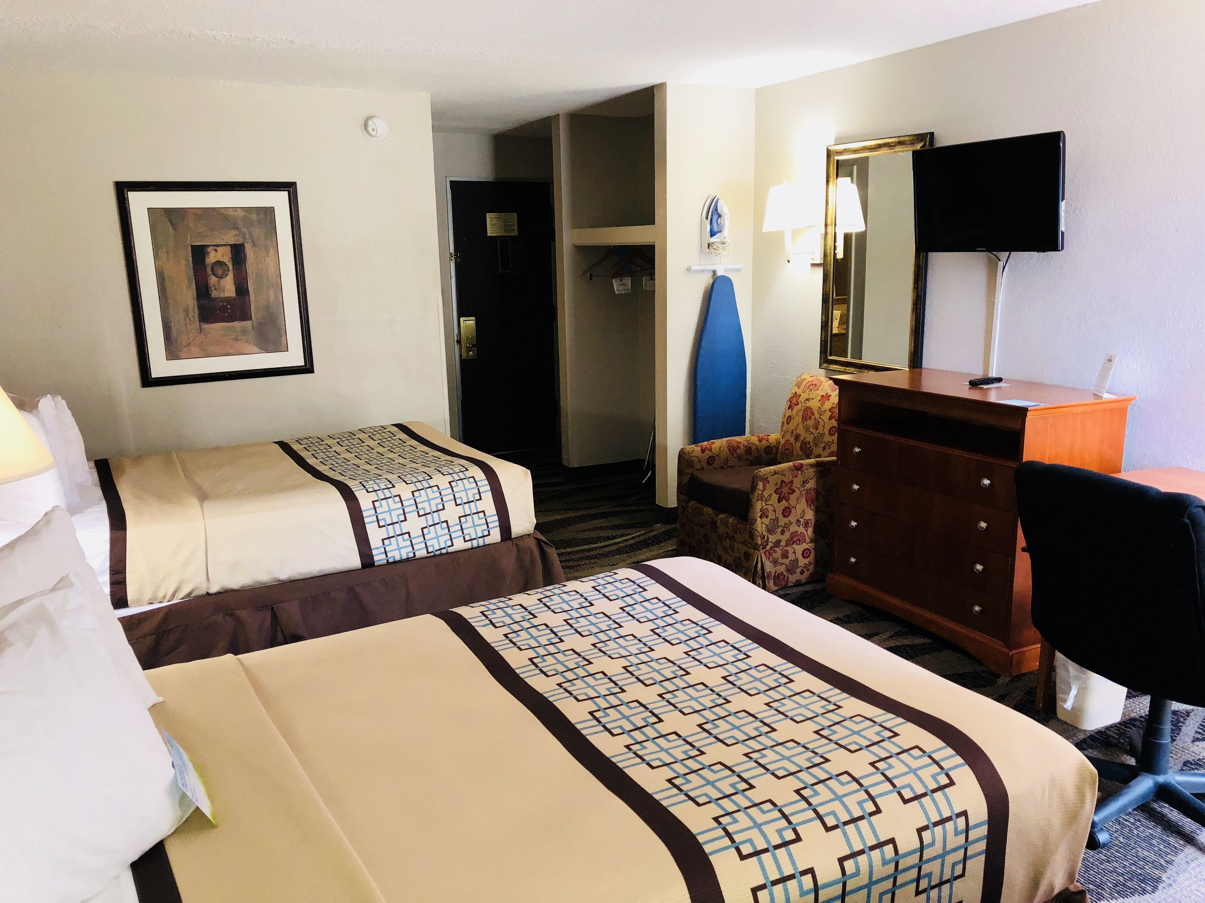 A hotel room with two beds, a desk, a chair, a dresser, a television, and a door leading to another room.