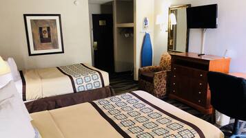 A hotel room with two beds, a desk, a chair, a dresser, a television, and a door leading to another room.