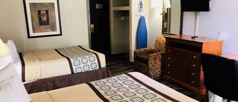 A hotel room with two beds, a desk, a chair, a dresser, a television, and a door leading to another room.