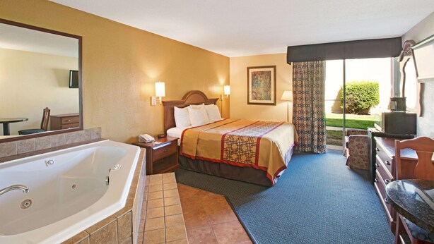 A hotel room with a large bed, a separate bathroom with a bathtub, a desk with a chair, and a television. - Days Inn by Wyndham Charlotte/Woodlawn Near Carowinds (Charlotte)