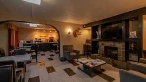 A hotel lobby with a dining area, seating, a fireplace, and a television. - Days Inn by Wyndham Charlotte/Woodlawn Near Carowinds (Charlotte)