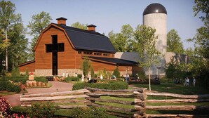 A wooden barn-like building with a large cross, surrounded by a landscaped garden and a silo. - Days Inn by Wyndham Charlotte/Woodlawn Near Carowinds (Charlotte)
