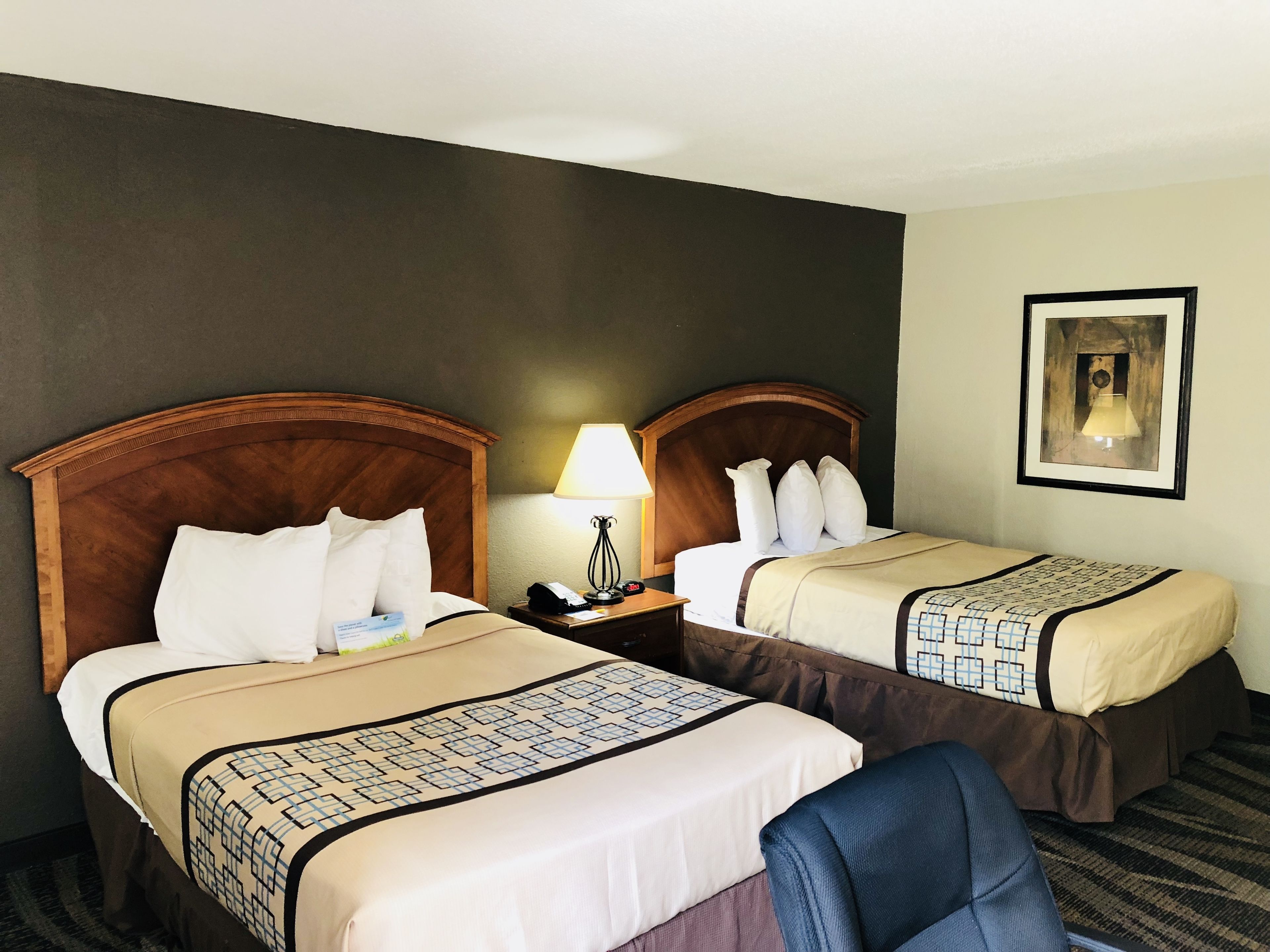 A hotel room with two beds, each with a wooden headboard, a bedside table with a lamp, and a framed picture on the wall.