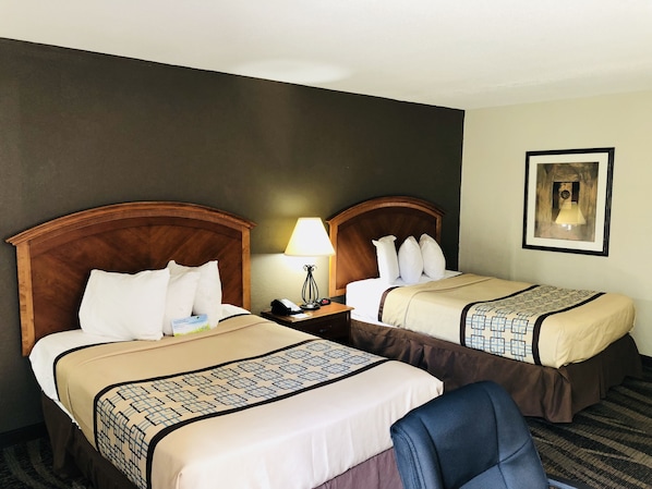 Une chambre d’hôtel avec deux lits, chacun doté d’une tête de lit en bois, d’une table de chevet avec une lampe et d’un tableau encadré au mur.