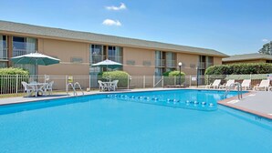 A swimming pool with lounge chairs and umbrellas, surrounded by a fence and a building with multiple windows and balconies. - Days Inn by Wyndham Charlotte/Woodlawn Near Carowinds (Charlotte)