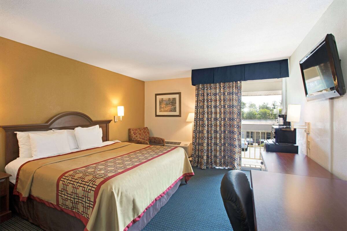 Habitación de hotel con una cama grande, un escritorio, una silla, un televisor y una ventana con cortinas.