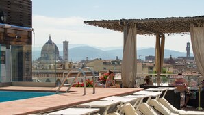 A rooftop pool area with lounge chairs, a pool, and a view of historic buildings and mountains. - Hotel Kraft (Florence)