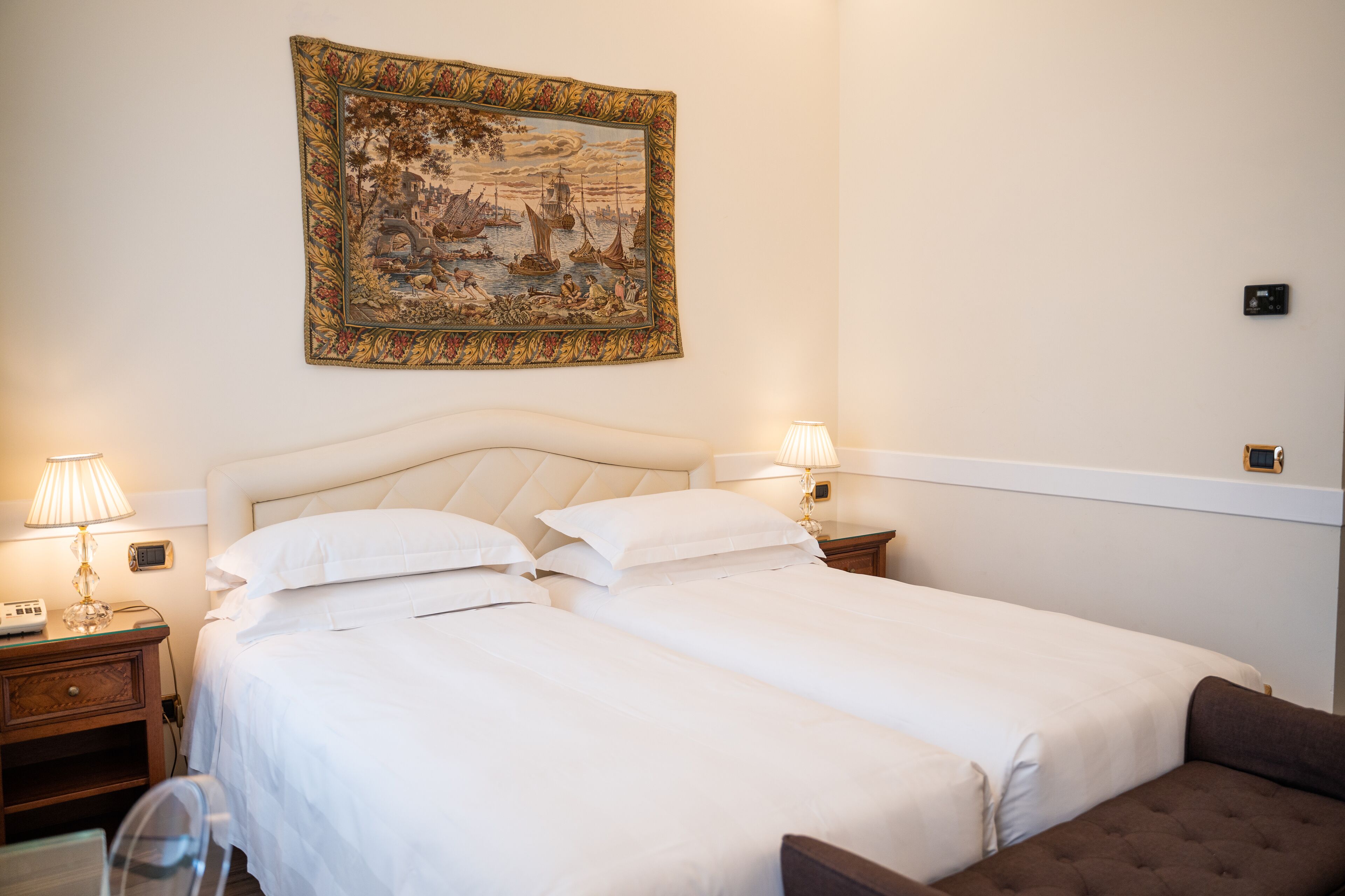 Una camera d'albergo con due letti, un comodino con lampada, un quadro appeso al muro e un tavolino.