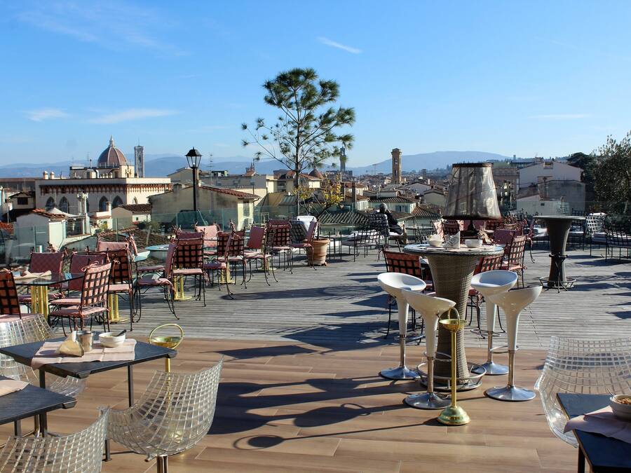 Un espacio de comedor al aire libre con mesas y sillas, una fuente y vistas de la ciudad al fondo.