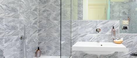 A modern bathroom with a marble shower, a sink, and a small stool.