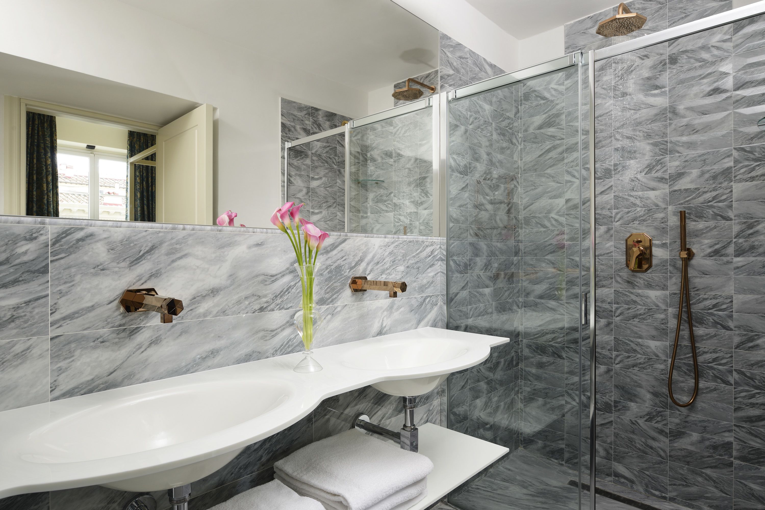 Une salle de bain moderne avec un pare-baignoire en marbre, un lavabo blanc et une douche à l’italienne.