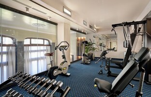 Una palestra alberghiera con attrezzature per esercizi, un pavimento a motivi blu e ampie finestre con tende.