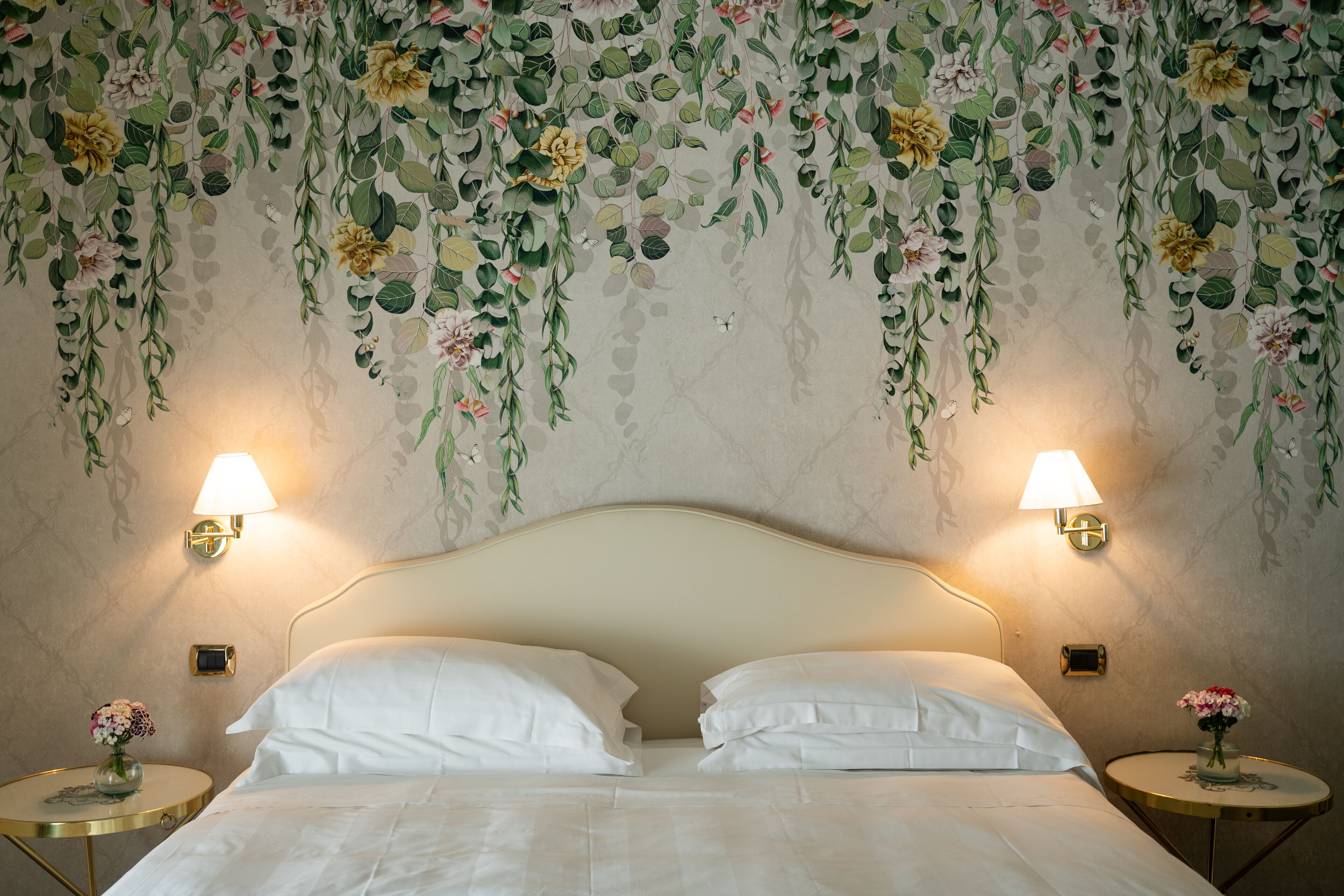 Une chambre d’hôtel avec un lit, deux tables de chevet avec des lampes et une décoration murale florale.