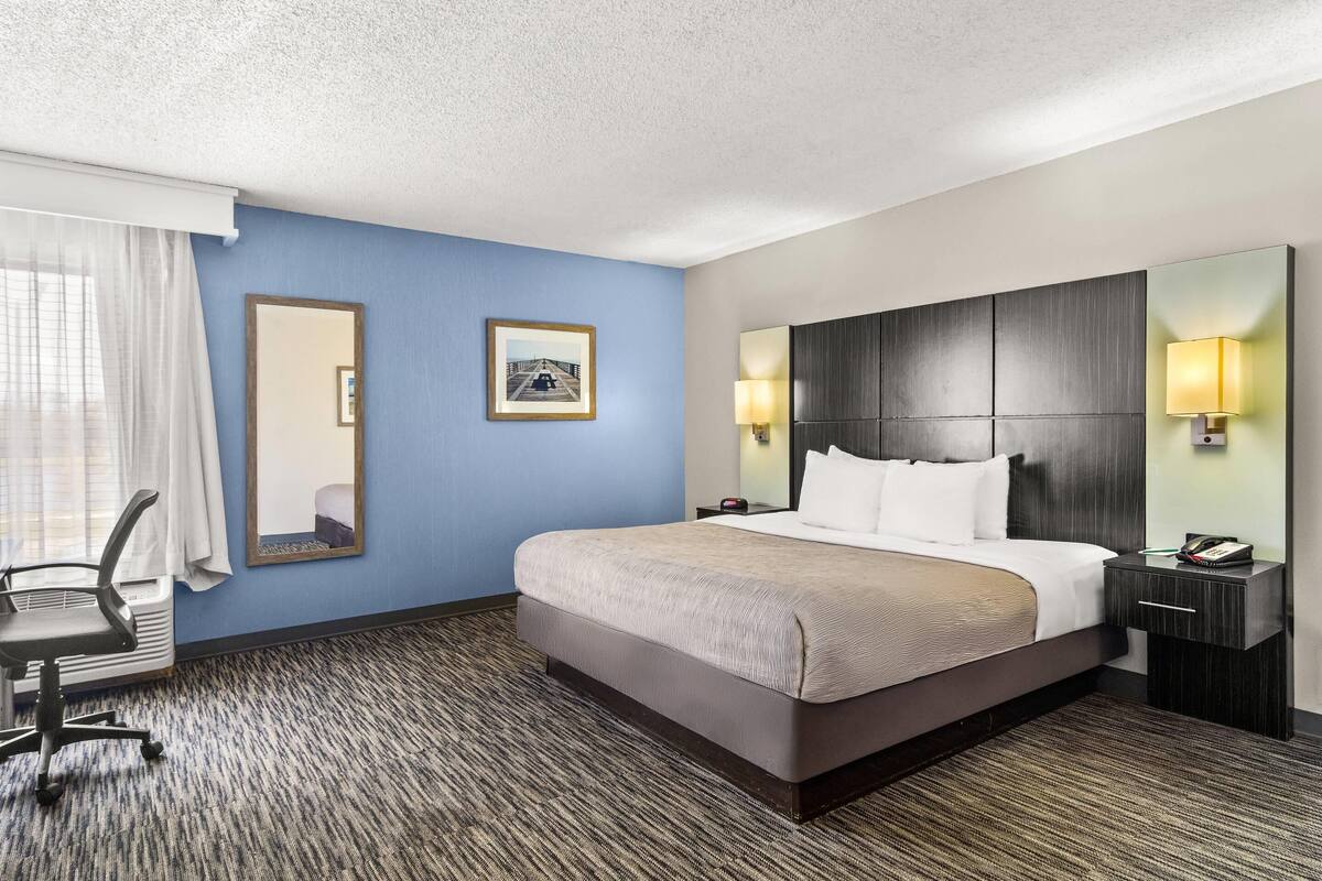 A hotel room with a large bed, a desk, a chair, a mirror, and two wall-mounted lamps.