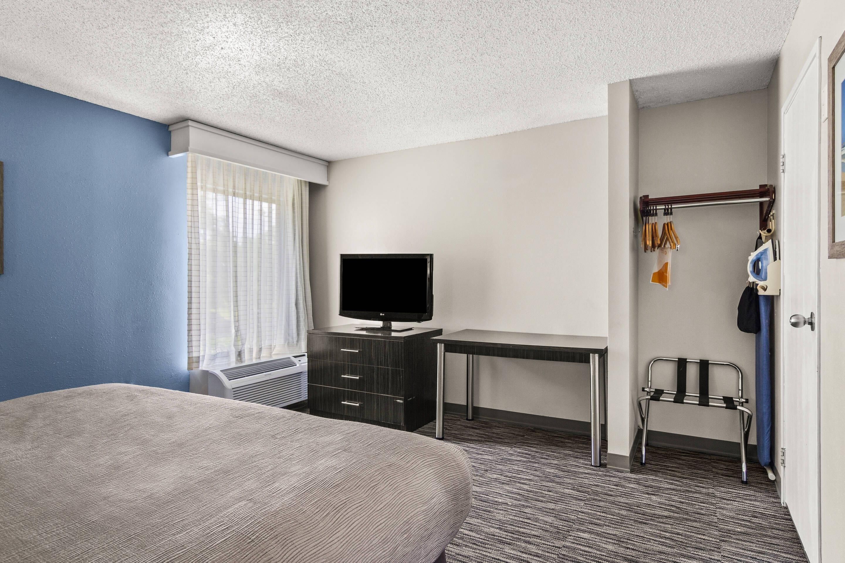 Habitación de hotel con cama, escritorio, televisión, perchero y ventana con cortinas.