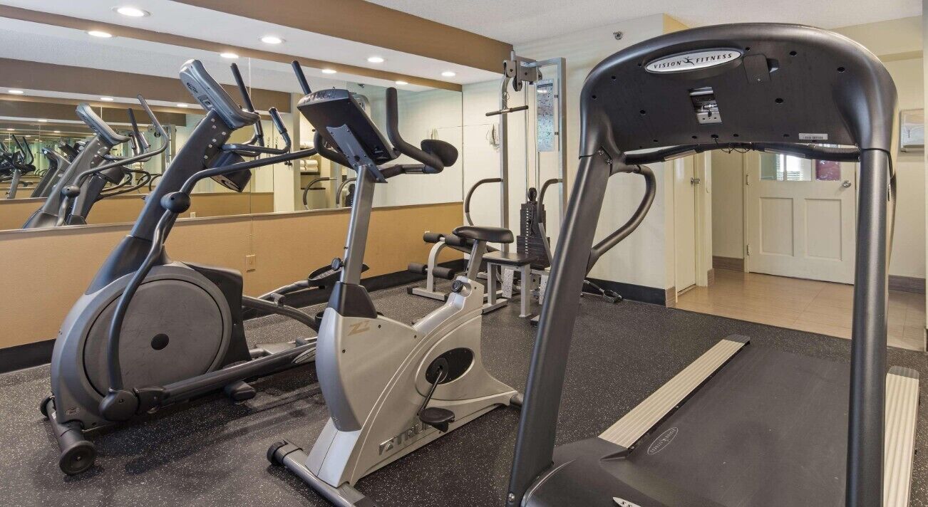 Een fitnessruimte met cardioapparaten, gewichten en een spiegelwand.