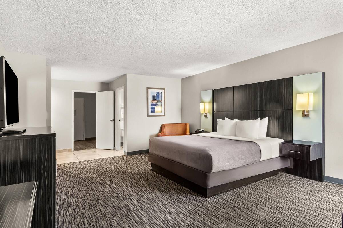 A hotel room with a large bed, a flat-screen TV, a desk, and a large mirror.