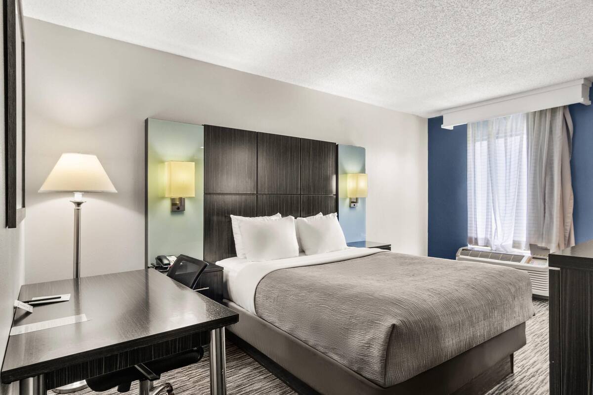 A hotel room with a large bed, bedside tables, a desk, a lamp, and a window with curtains.