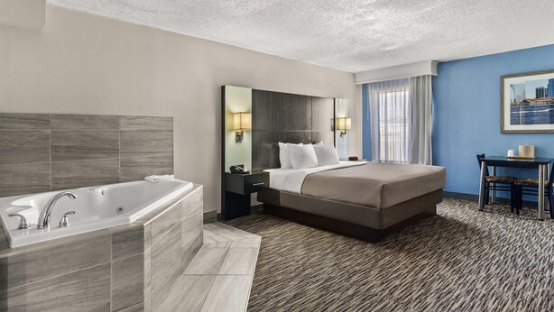 Habitación de hotel con una cama grande, baño independiente con bañera, escritorio con silla y un cuadro de un paisaje urbano en la pared.