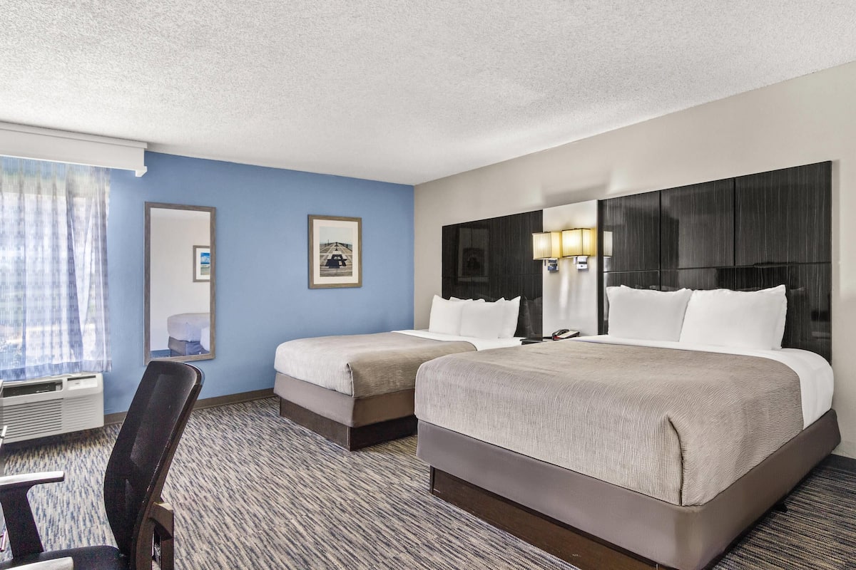 A hotel room with two beds, a desk, a chair, a large mirror, and a window with curtains.