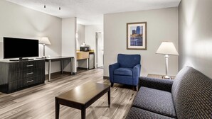 Una habitación de hotel moderna con una televisión de pantalla plana, un sofá, una mesa de comedor, un ventilador de techo y una cocina al fondo.