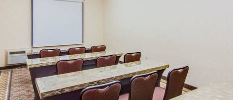 A conference room with a long table, patterned chairs, a projector screen, and a carpeted floor.