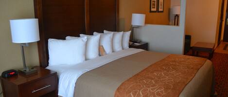 A hotel room with a large bed, two bedside tables with lamps, a wooden headboard, and a carpeted floor.