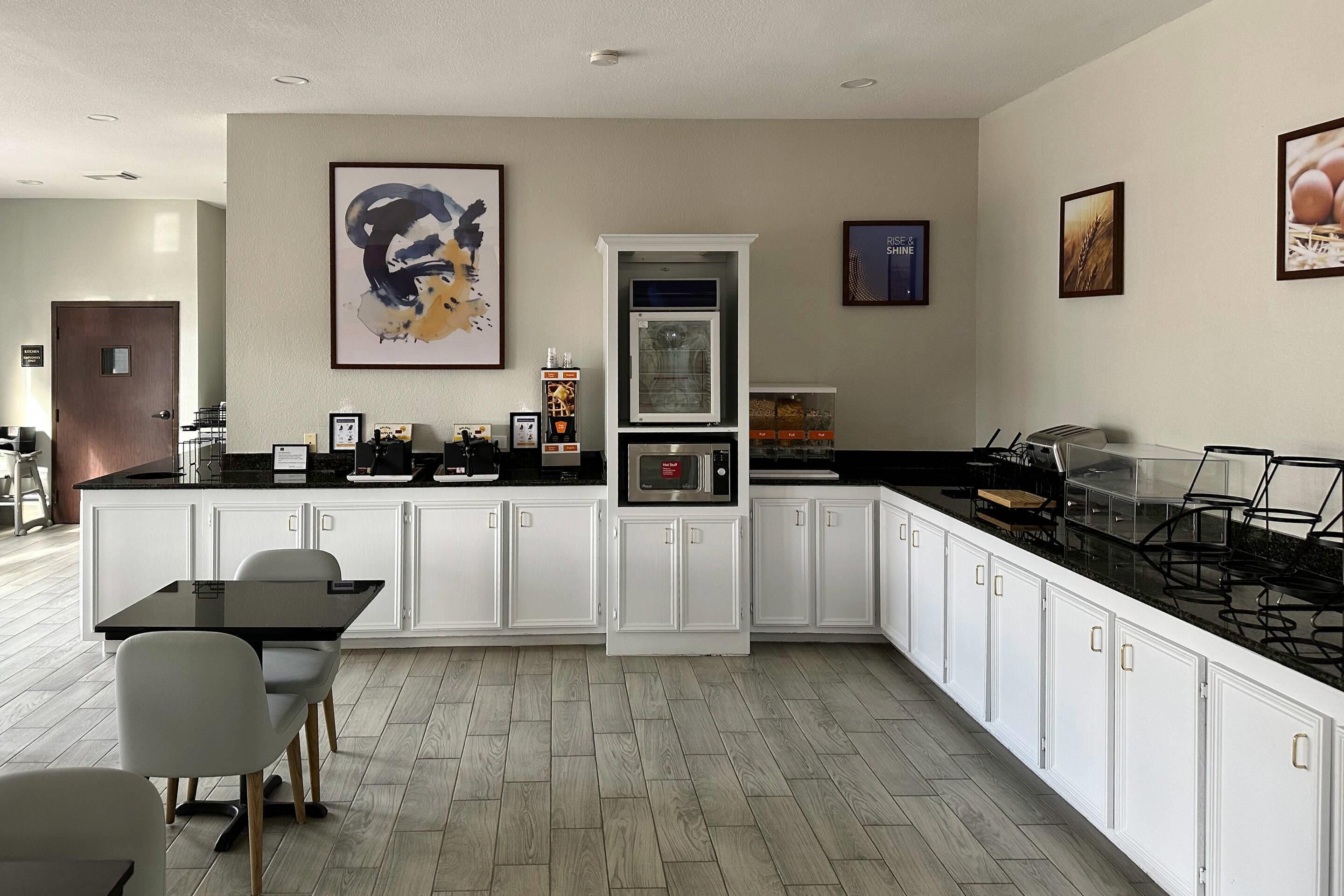 A modern kitchen with white cabinetry, a black countertop, and a dining area with a glass table and chairs.