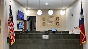A hotel reception area with a sign reading "Comfort Inn & Suites," a digital screen, and two flags. - Comfort Inn & Suites Houston Key-Katy (Katy)