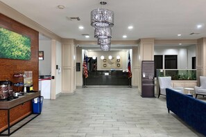 Zona de recepción de un hotel con un mostrador de madera, un candelabro, banderas y un área de descanso con un sofá azul.