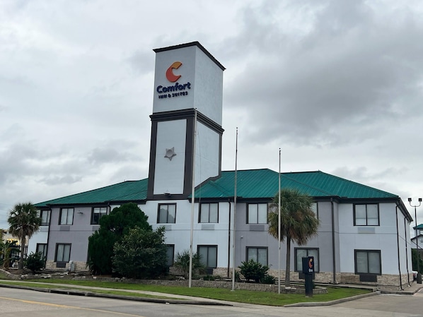 Un hotel Comfort Inn & Suites con diseño moderno, que destaca una torre prominente con el logotipo del hotel, techo verde y un césped delantero cuidado.