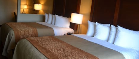 A hotel room with two beds, each with a headboard, a bedside table, and a lamp.