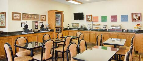 Un comedor de hotel con mesas y sillas, un mostrador de buffet y un refrigerador.