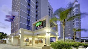 Un hotel Courtyard Marriott con diseño moderno, que destaca un letrero llamativo, varios pisos y una entrada bien iluminada.