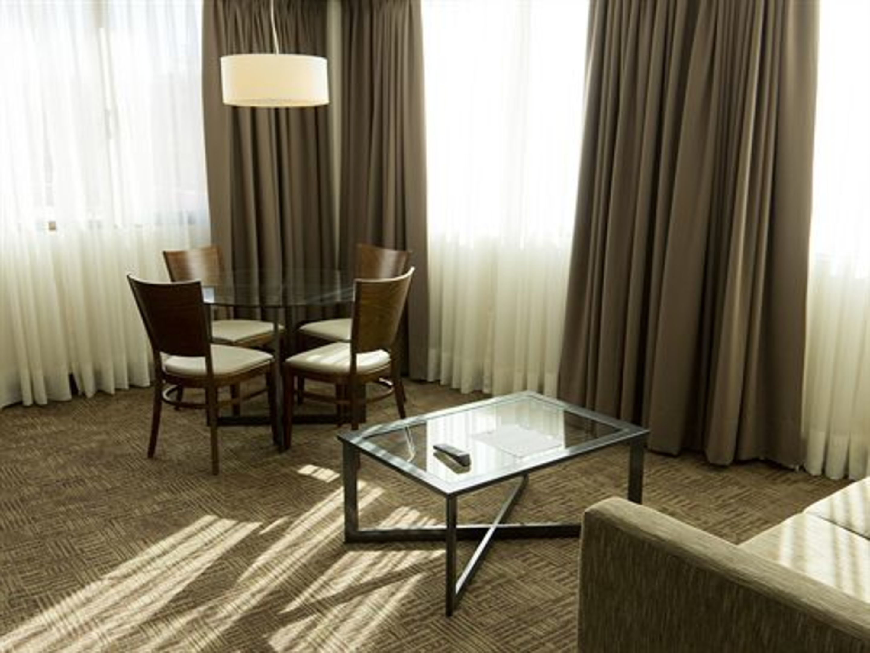 Une chambre d’hôtel avec une table à plateau en verre, deux chaises, un canapé et une lampe.