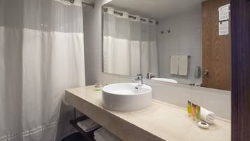 Un baño con lavamanos blanco, espejo y cortina de ducha.