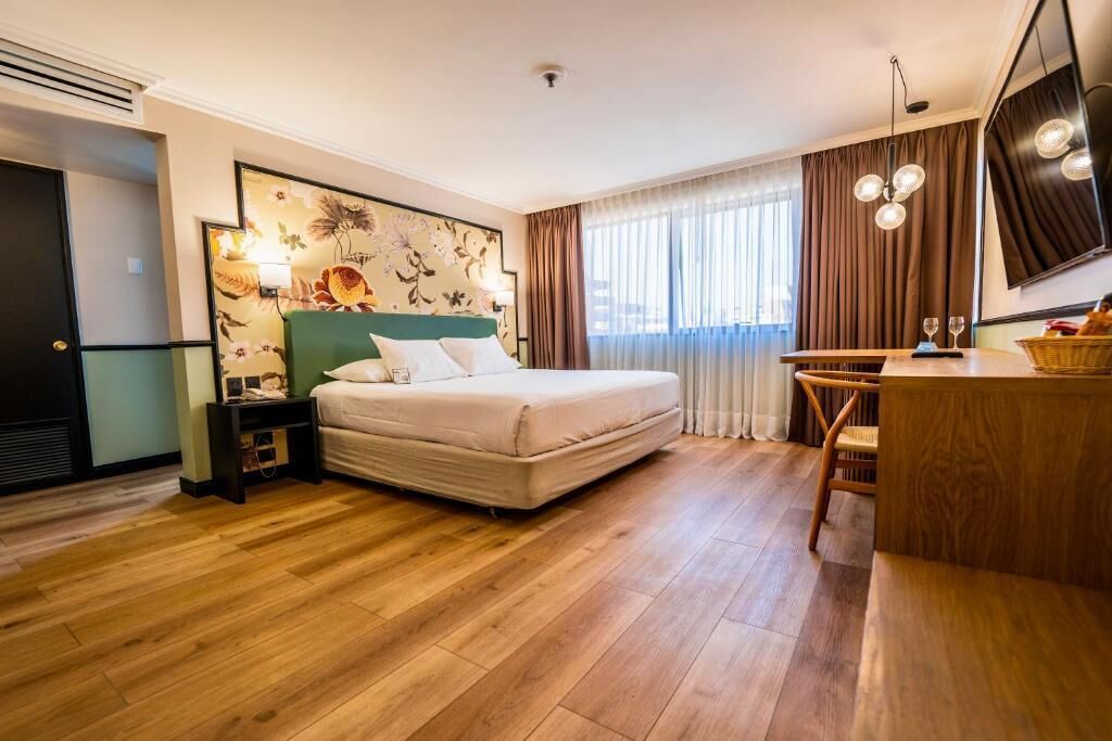 Una camera d'albergo con un letto, una scrivania, una sedia, una televisione e una finestra con tende.