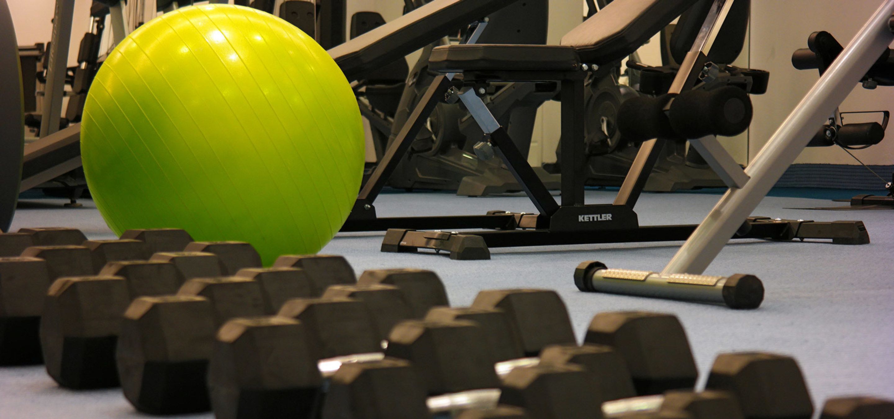 Een sportschool met trainingsapparatuur, waaronder gewichten en een kettlebell.